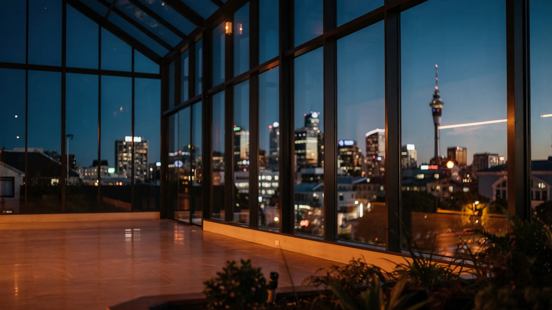 Evening view through the glass of a modern glasshouse towards the Auckland skyline